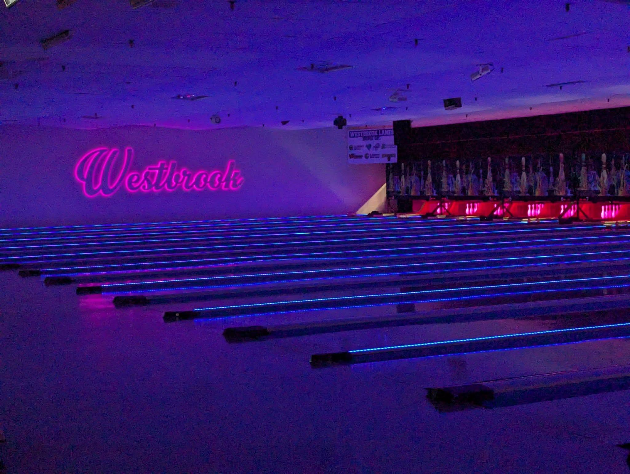 Cosmic bowling under neon lights at Westbrook Lanes — glowing blue lanes and pink Westbrook sign